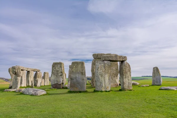Etrafında yeşil çimenler, mavi gökyüzü ve bulutlar olan Stonehenge.