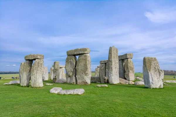 Arkasında yeşil çimenler ve bulutlu mavi gökyüzü olan Stonehenge