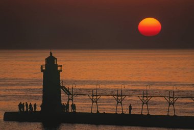 South Haven, Michigan deniz feneri, podyum ve siluetli insanlarla dolu iskele günbatımında manzara, Michigan Gölü, ABD