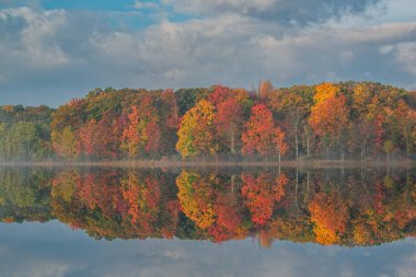 Autumn landscape of the shoreline of Deep Lake at sunrise with mirrored reflections in calm water, Yankee Springs State Park, Michigan, USA