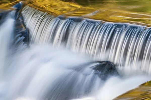 位于美国密歇根州上半岛的邦德瀑布瀑布上 一道瀑布的景观闪烁着模糊的光 被来自阳光灿烂的秋天枫树和头顶蓝天的反光照亮 — 图库照片