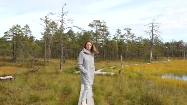 Young happy woman walking on wooden boardwalk through bog swamp land — Stock Video