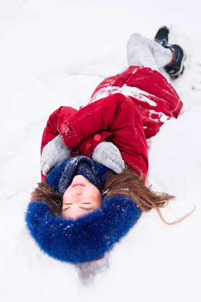 En ung, lykkelig kvinne i rød frakk som ligger på snøen – stockfoto