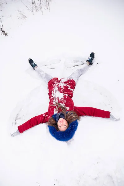 Jonge grappige vrouw in rode jas liggend op de sneeuw — Stockfoto