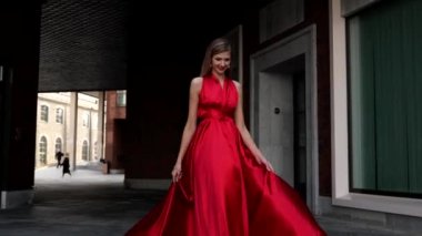 Şehirde uzun kırmızı elbiseli genç ve güzel bir kadın yürüyor.