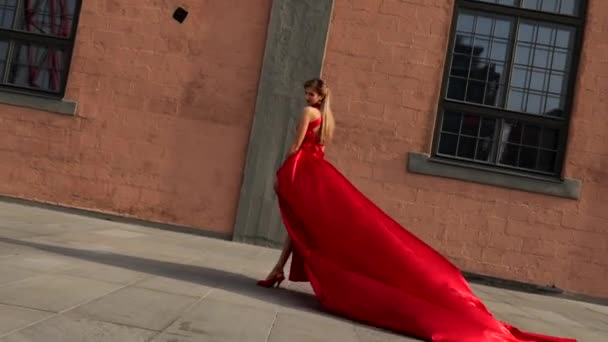 Mujer hermosa joven en vestido rojo largo caminando en la ciudad — Vídeo de stock
