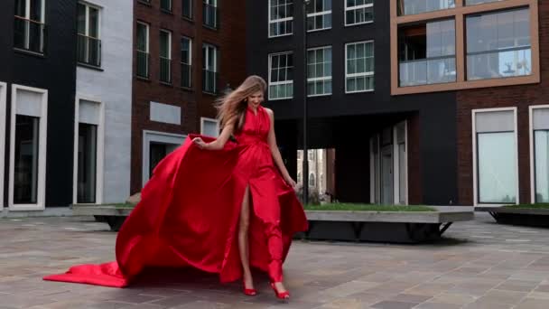 Junge hinreißende Frau im langen roten Kleid spaziert durch die Stadt — Stockvideo