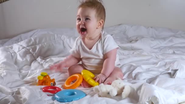 Schattig acht maanden oud meisje spelen met piramide speelgoed zitten op het bed — Stockvideo