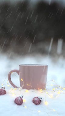 Karda noel topları olan bir bardak sıcak içecek.