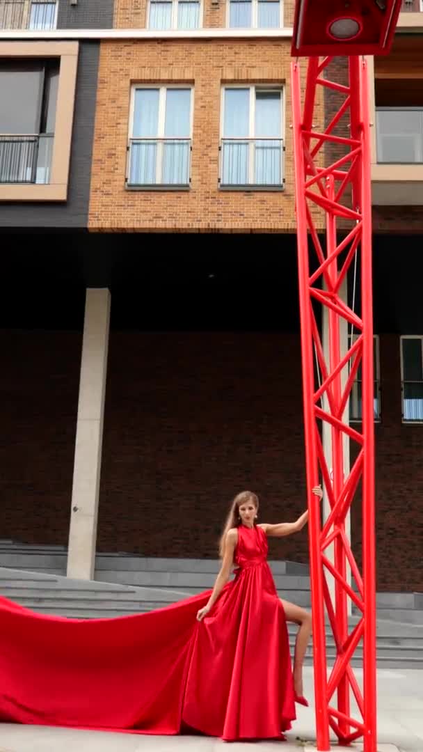 Mladá nádherná žena v dlouhých červených šatech stojící v blízkosti červené lampy — Stock video