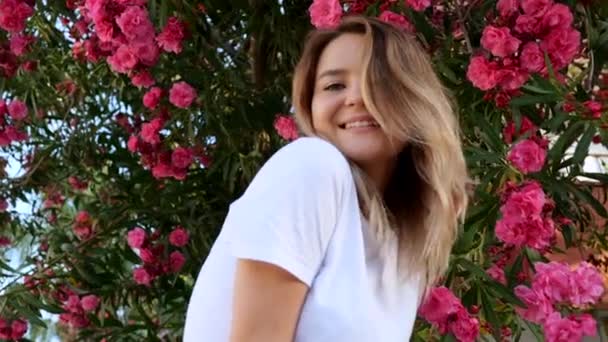 Молода жінка в білій сорочці з натуральним макіяжем, що стоїть у квітучому кущі — стокове відео