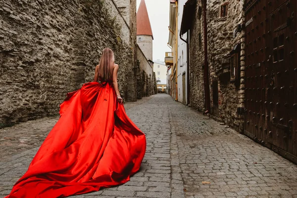 Jeune femme magnifique en robe rouge longue marchant dans la ville médiévale — Photo