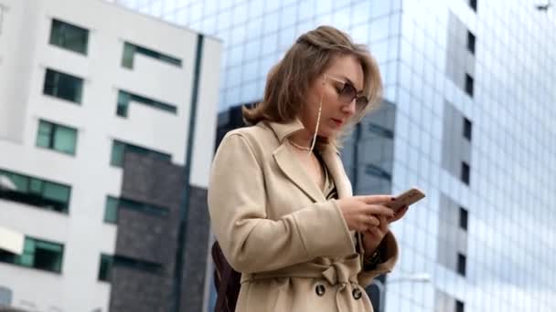 Young business woman wearing beige coat standing on the street holding phone — Stock Video