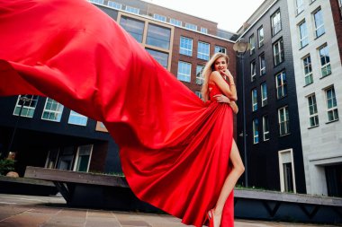 Modern şehirde poz veren uzun kırmızı elbiseli muhteşem bir kadın.