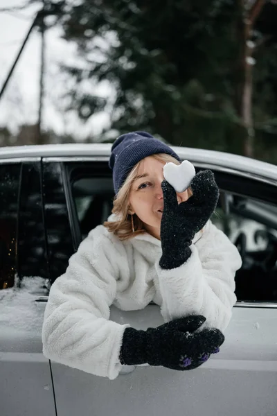 Happy woman in stylish winter clothes hiding behind heart shape snow ball – stockfoto