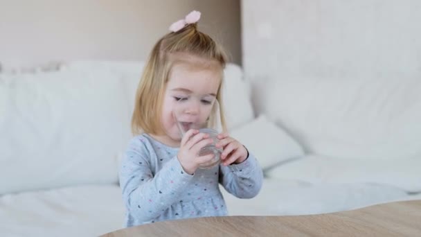 Чарівна 1,5-річна дівчина п'є воду зі скла — стокове відео