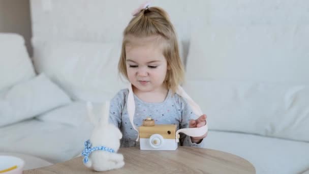 Kleines entzückendes Mädchen spielt mit Holzspielzeug-Kamera und flauschigem Kaninchen-Spielzeug — Stockvideo