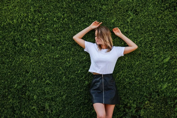 Jonge vrouw in wit shirt en korte zwarte rok staan door groenblijvende heg — Stockfoto