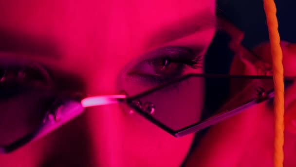 穿着时髦的霓虹灯、红光和粉红光的年轻漂亮女性眼睛的特写 — 图库视频影像