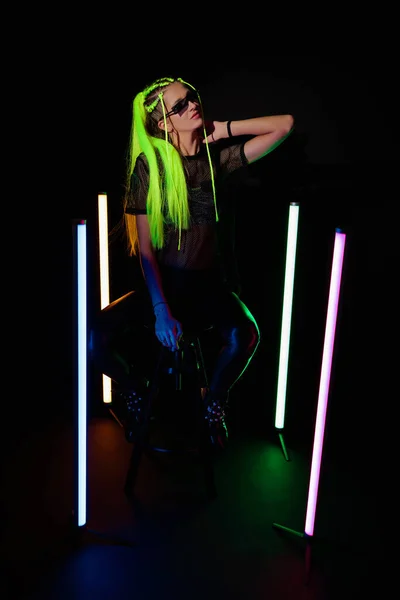 Mladá atraktivní žena se žlutými vlasy sedí v blízkosti barevné neonové trubice světla — Stock fotografie