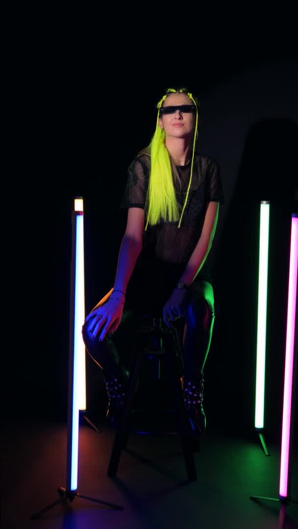 Jovem mulher atraente com cabelo amarelo sentado perto de luzes coloridas tubo de néon — Vídeo de Stock