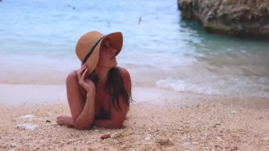 Hasır şapkalı güzel bir kadın sahile yakın kumsalda oturmuş hayatının tadını çıkarıyor. Denizde yaz tatili