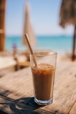 Plajda buzlu kahve. Plaj barında, deniz kenarında samanla birlikte uzun bardakta buzlu kahve.