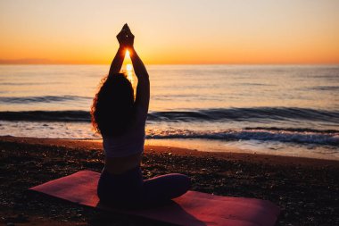 Backside view of calm woman yoga practicing by the sea sunrise time. Finding inner peace spiritual healing lifestyle.