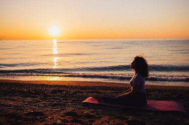 Calm woman yoga practicing meditating by the sea sunrise time. Finding inner peace, spiritual healing lifestyle.