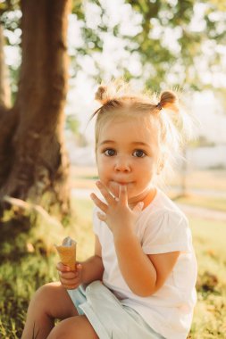 Adorable 2 years old girl eating ice cream outdoors at park, summer time