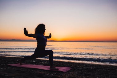 Backside view of calm woman yoga practicing by the sea sunrise time. Finding inner peace spiritual healing lifestyle.