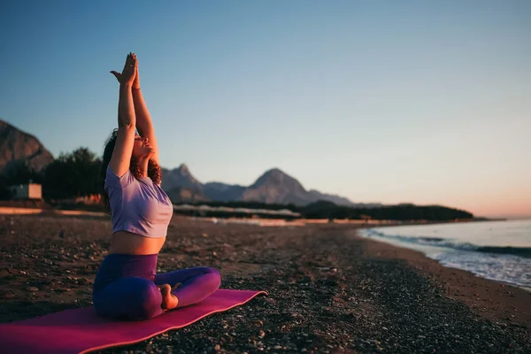 Carefree woman sitting in yoga mountain pose by the sea sunrise time. Finding inner peace spiritual healing lifestyle. Stretching in the morning for increasing energy.