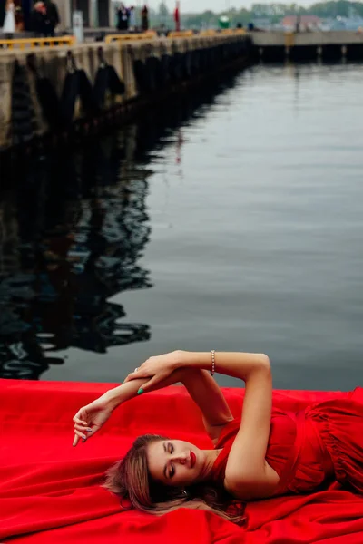 若いです魅力的な女性で長い赤いドレスと赤い靴木製の桟橋に横たわって — ストック写真