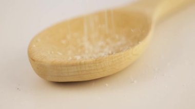 Close-up of coconut shavings sprinkled from above into a wooden scoop. 