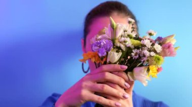 Young woman hides behind a bouquet spring flowers on blue background