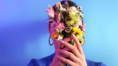 Young woman hides behind a bouquet spring flowers on blue background
