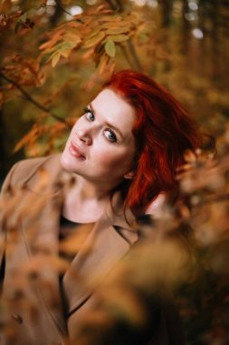 Renkli sonbahar yapraklarının yanında duran ve kameraya bakan boyalı kızıl saçlı, delinmiş burunlu güzel bir sonbahar kadınının yakın plan portresi. Güzel bir kadın bireyselliğini gösteriyor.. 