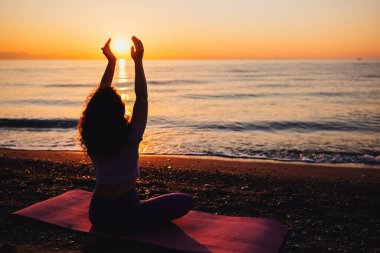Backside view of calm woman yoga practicing by the sea sunrise time. Finding inner peace spiritual healing lifestyle.