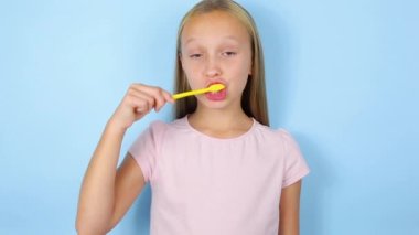 Kız mavi bir arka planda dişlerini fırçalıyor. Ağız bakımı