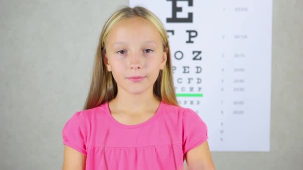 एक अच्छा मूड में लड़की एक ऑप्थाल्मोलॉजिस्ट में दृष्टि सुधार के लिए चश्मा पर कोशिश करती है — स्टॉक वीडियो