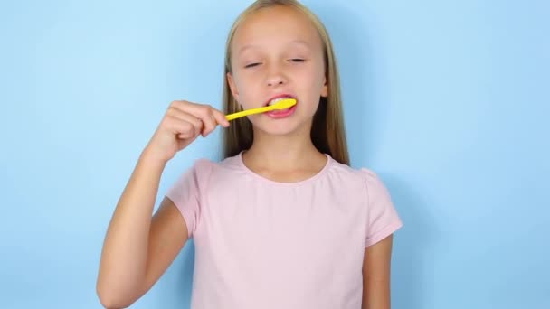 La chica se cepilla los dientes sobre un fondo azul de cerca. Cuidado oral — Vídeos de Stock