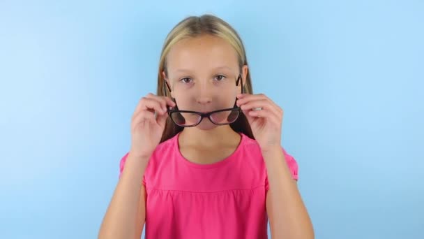 Дівчина в хорошому настрої на синьому фоні одягає окуляри для виправлення зору . — стокове відео