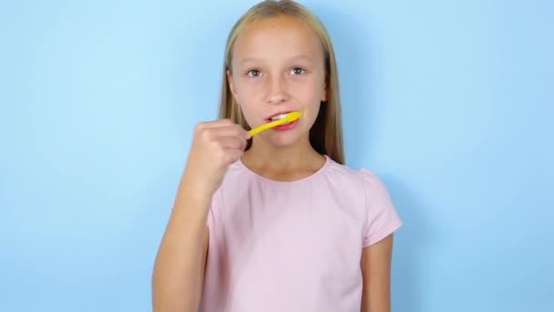 Дівчина чистить зуби на синьому фоні крупним планом. Усна допомога — стокове відео
