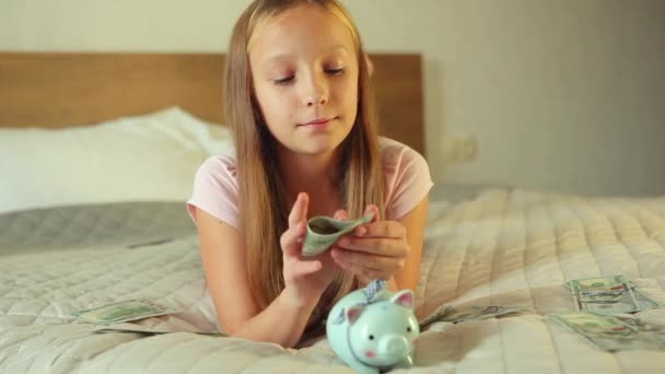Подростковая девушка кладет счета в копилку свиньи в домашнем интерьере — стоковое видео