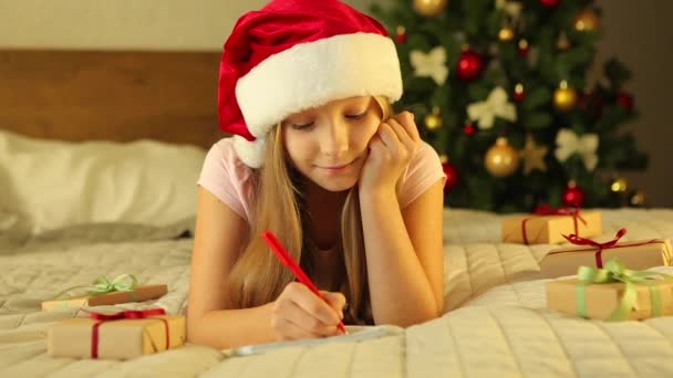 Criança em um interior decorado para o Natal escreve uma carta ao Papai Noel — Vídeo de Stock