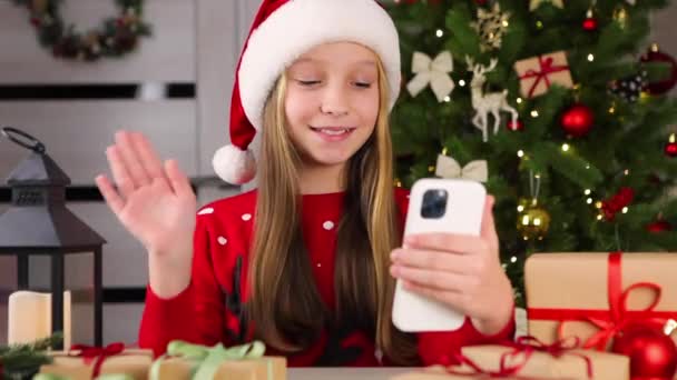Dziewczyna komunikuje się za pośrednictwem połączenia wideo za pomocą smartfona we wnętrzu Bożego Narodzenia — Wideo stockowe