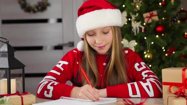 Noel için dekore edilmiş bir iç mekandaki çocuk Noel Baba 'ya bir mektup yazar. — Stok video