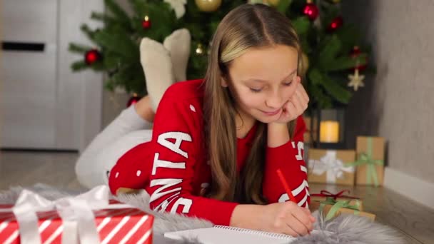 Enfant dans un intérieur décoré pour Noël écrit une lettre au Père Noël — Video