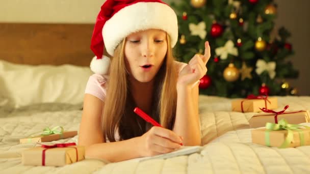 Bambino in un interno decorato per Natale scrive una lettera a Babbo Natale — Video Stock
