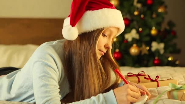 Barn i en dekorerad inredning för jul skriver ett brev till jultomten — Stockvideo